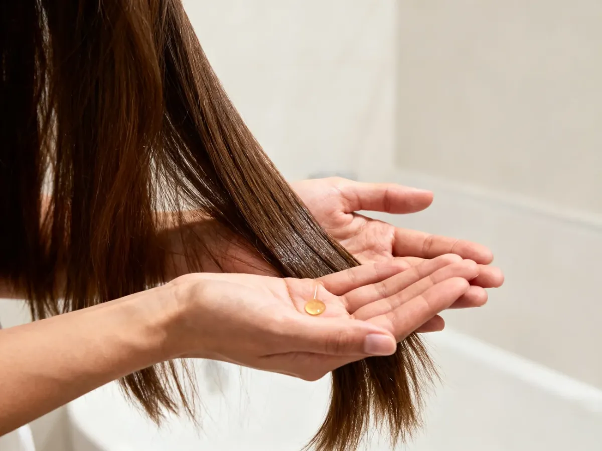 A person applying serum sparingly to the lengths and ends of their hair